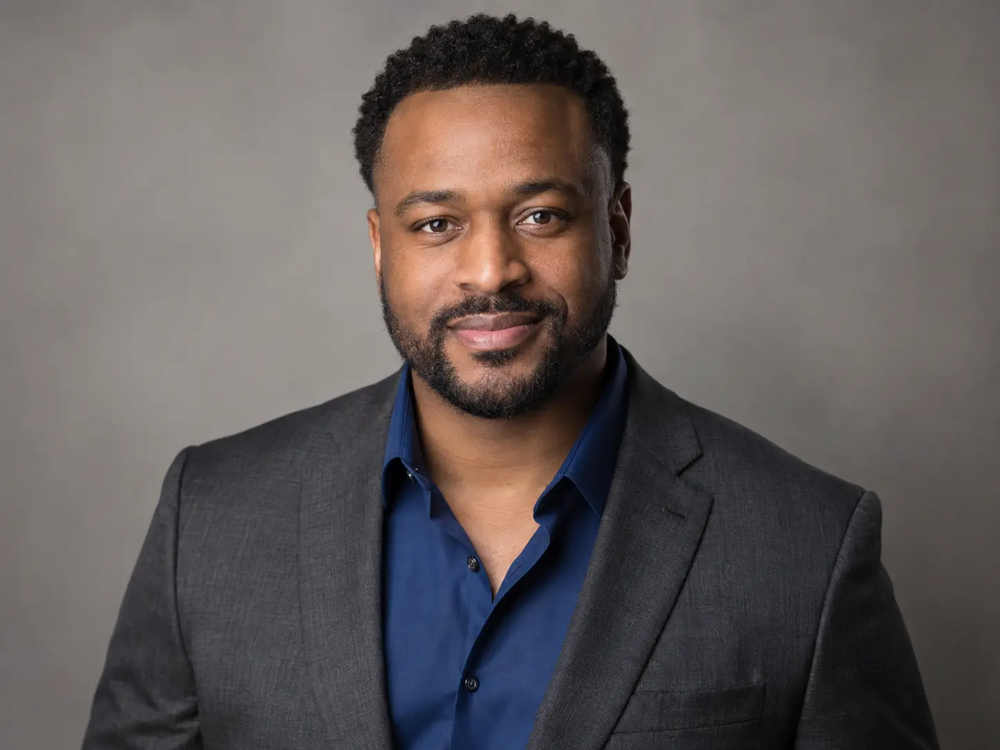 Professional corporate headshot of a man in a charcoal blazer