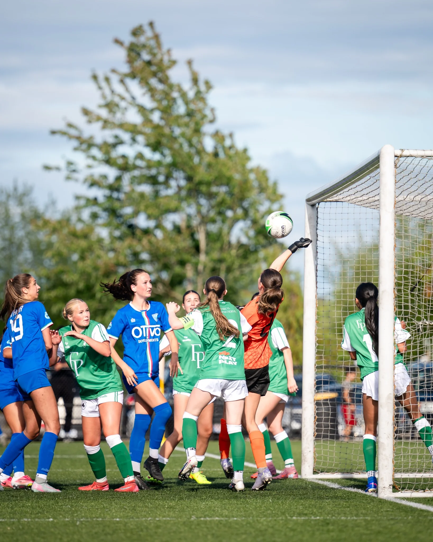 Soccer goalkeeper reaching for the ball amid players near the goal